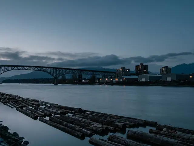 River at dusk with a log boom and a truss bridge