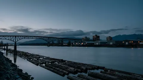River at dusk with a log boom and a truss bridge